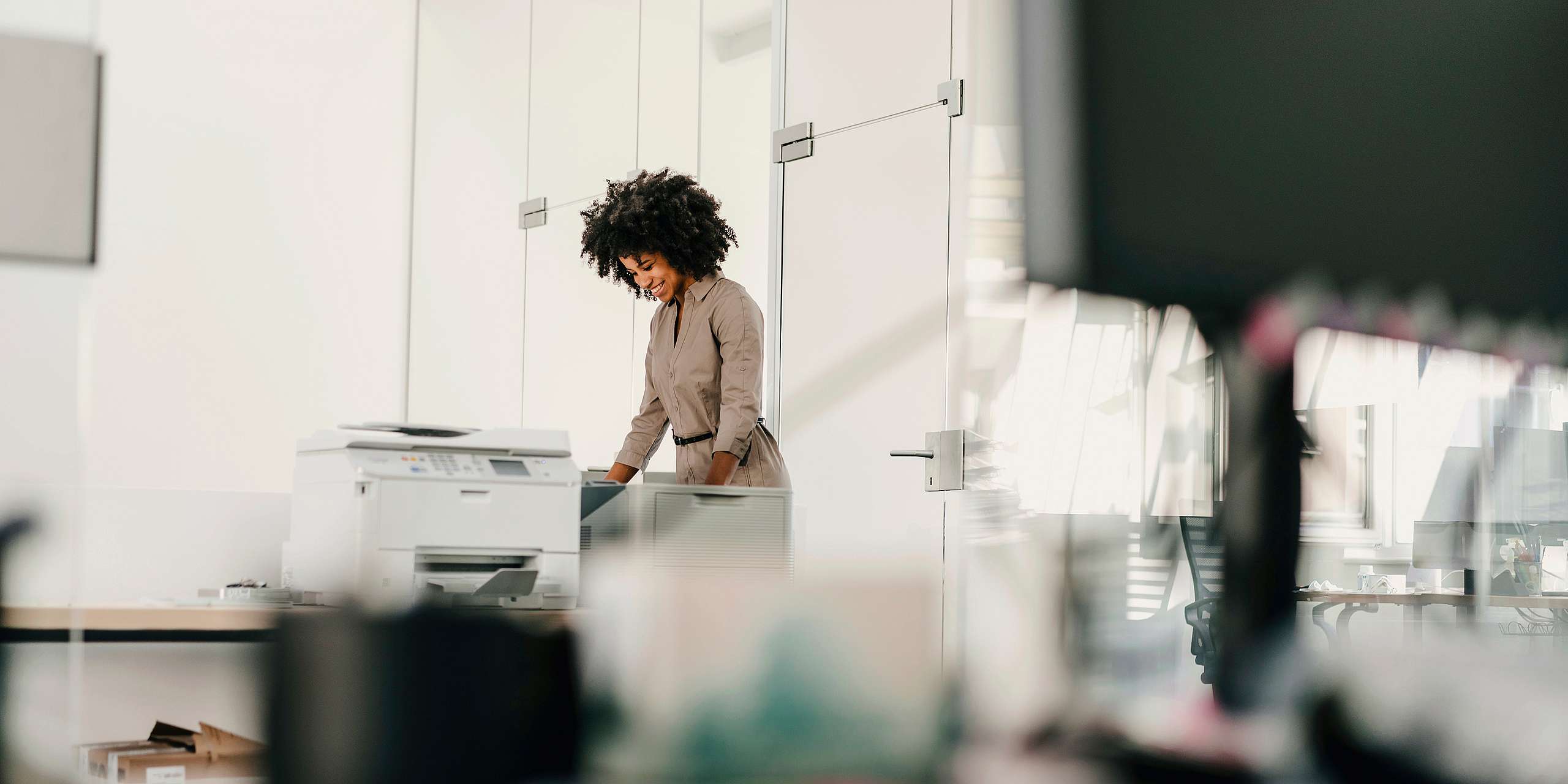 Young businesswoman in modern office smiling while using a photocopier, highlighting equipment safety and lease responsibilities.
