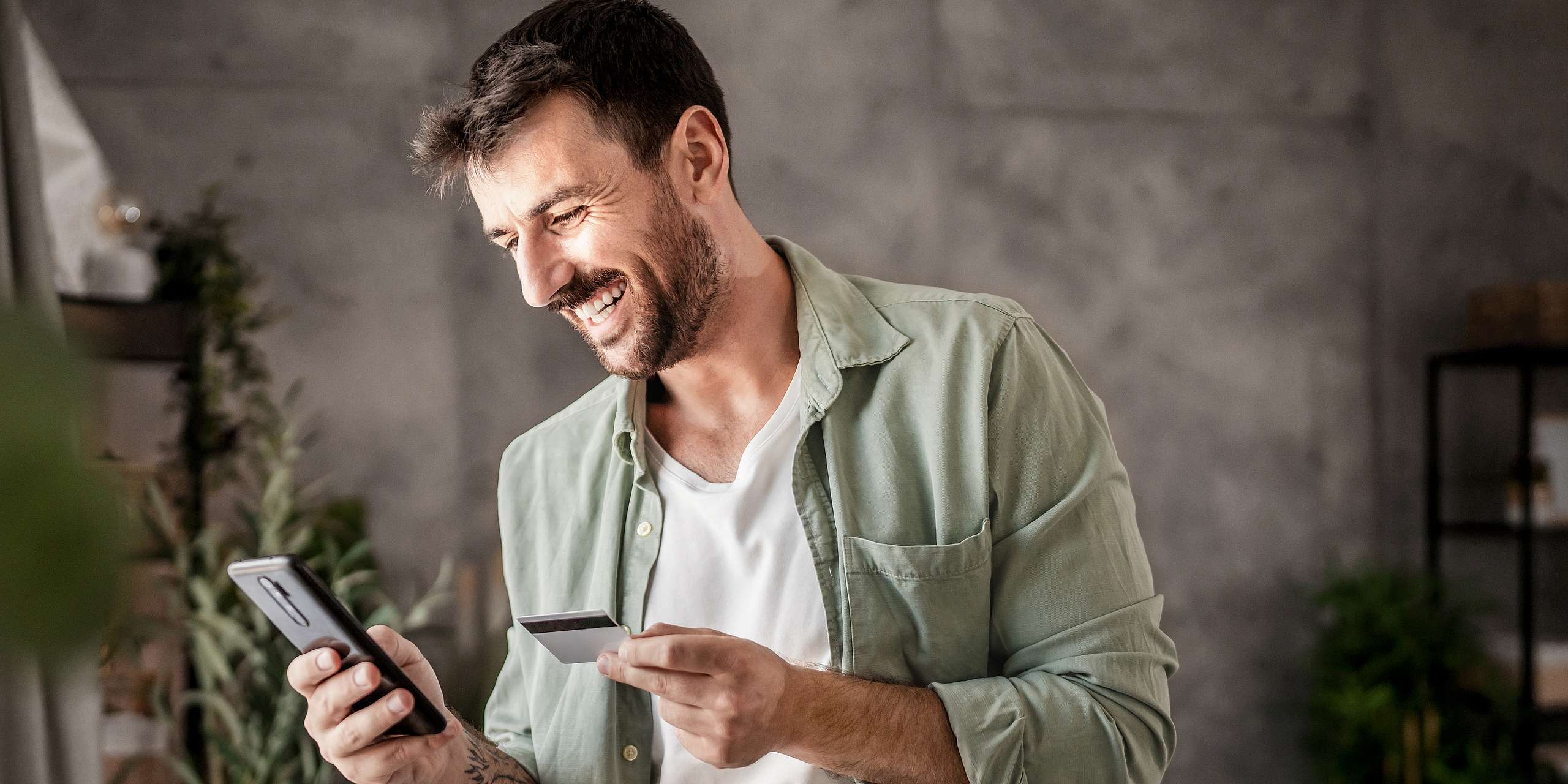 A man smiling as he completes a task on his phone with his credit card.
