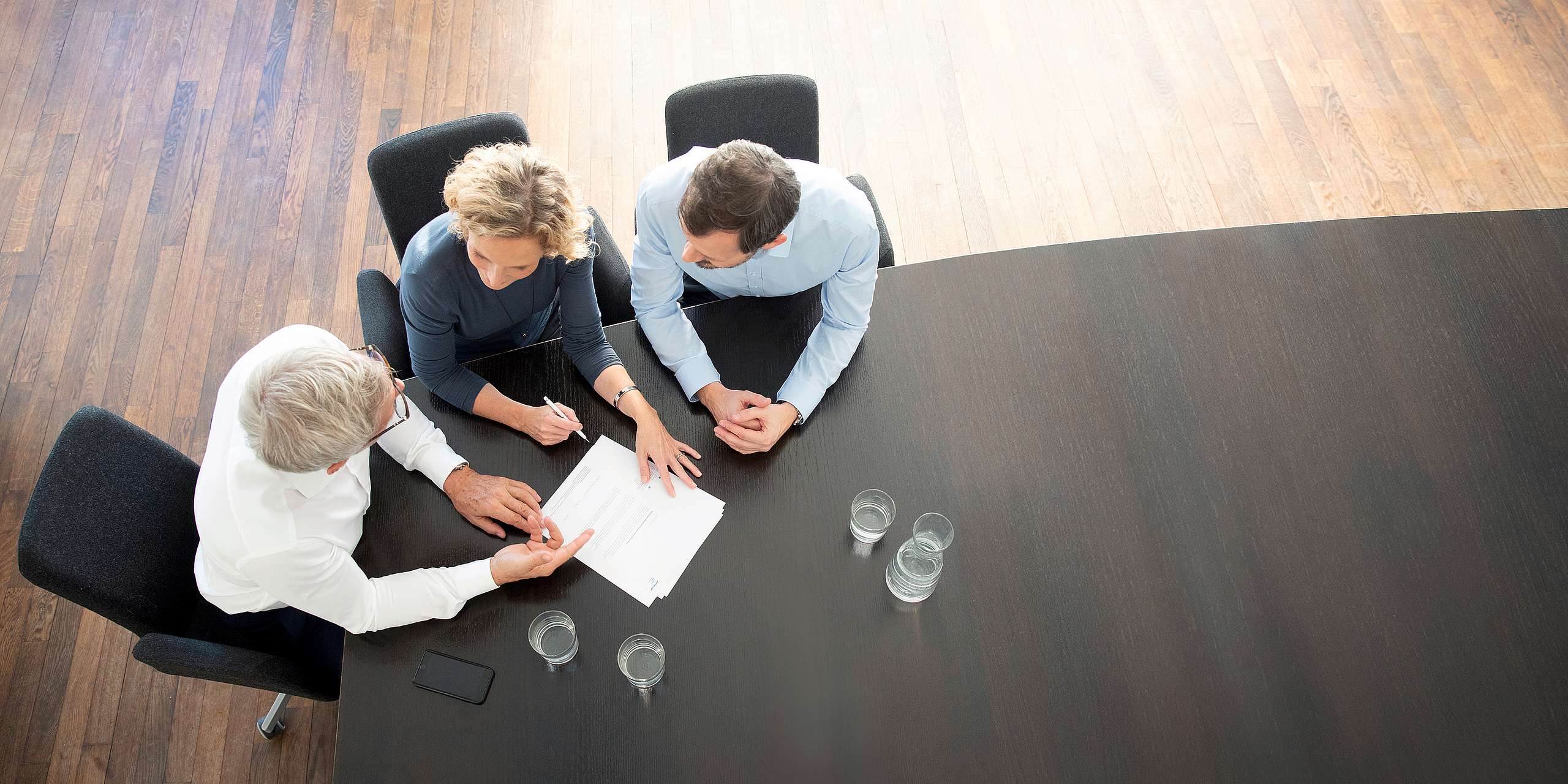 Aerial view of three business people in a boardroom discussing equipment and service with their chosen equipment supplier.