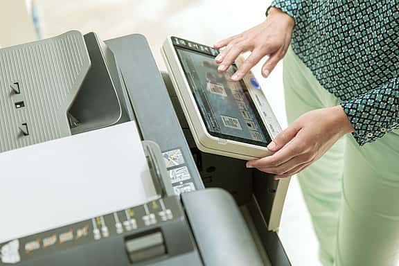 Close-up of hands using a photocopier, ensuring equipment is in good working order before signing the Delivery Certificate to begin the lease.
