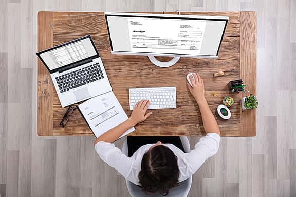 A person at their desk with an IT hardware setup, including a computer, keyboard, mouse, and laptop, illustrating grenke's flexible financing options for upgrading computer systems, servers, and networking equipment.