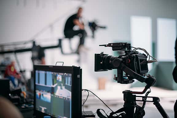 Close-up of a media shooting setup with a camera, filming software on a screen, and a film crew controlling sound and set in the background, highlighting grenke's financing options for audiovisual equipment, also including projectors, sound systems, and video conferencing tools.