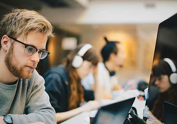 Man using computer in busy office, highlighting equipment upgrade options, new hire agreements, and seamless contract transitions facilitated by grenke.