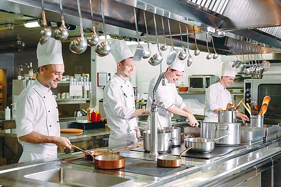 Professional chefs in an industrial kitchen setting, illustrating grenke's financing solutions for top-of-the-line catering equipment including ovens, refrigerators, prep stations, and dishwashers.