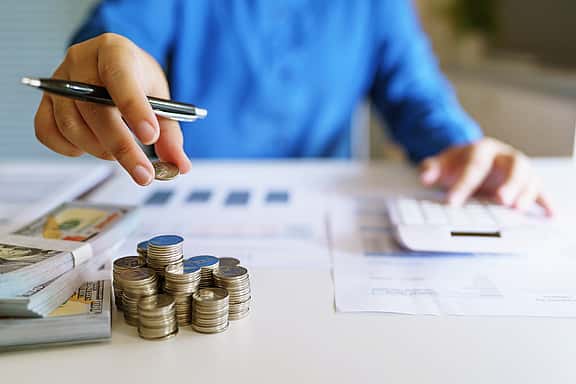 A small business owner is counting money with calculator, looking into the business' budgets and finances.