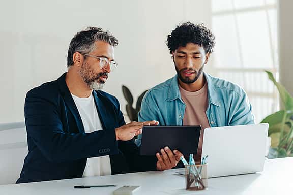A woman showing her iPad screen to two focused and delighted men, discussing grenke's finance solutions and how the reseller toolkit supports achieving more sales and business success.