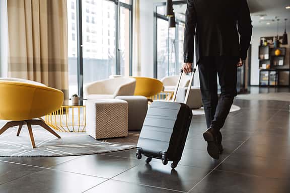 Person walking through a hotel lobby with a suitcase, showcasing grenke's financing options for hospitality equipment, including commercial kitchen appliances and guest room furnishings, to enhance guest experiences.