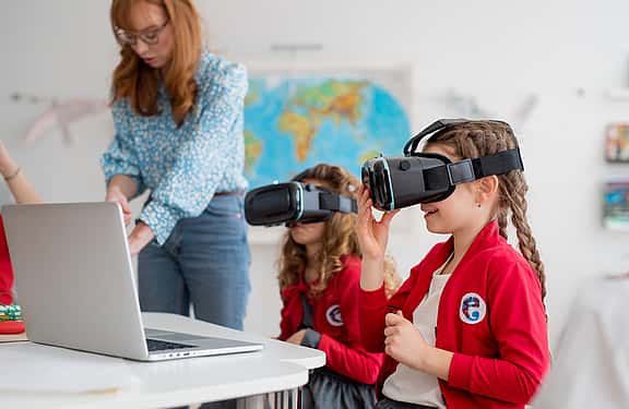 Two young girls in school uniforms using a VR headset in a classroom, showcasing grenke's financing options for educational technology, also including interactive whiteboards and laboratory equipment, to enhance learning experiences.