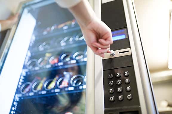 Close-up of hands pressing a button on a vending machine, showcasing grenke's financing solutions for snack and beverage machines, as well as specialised vending units for businesses and facilities.