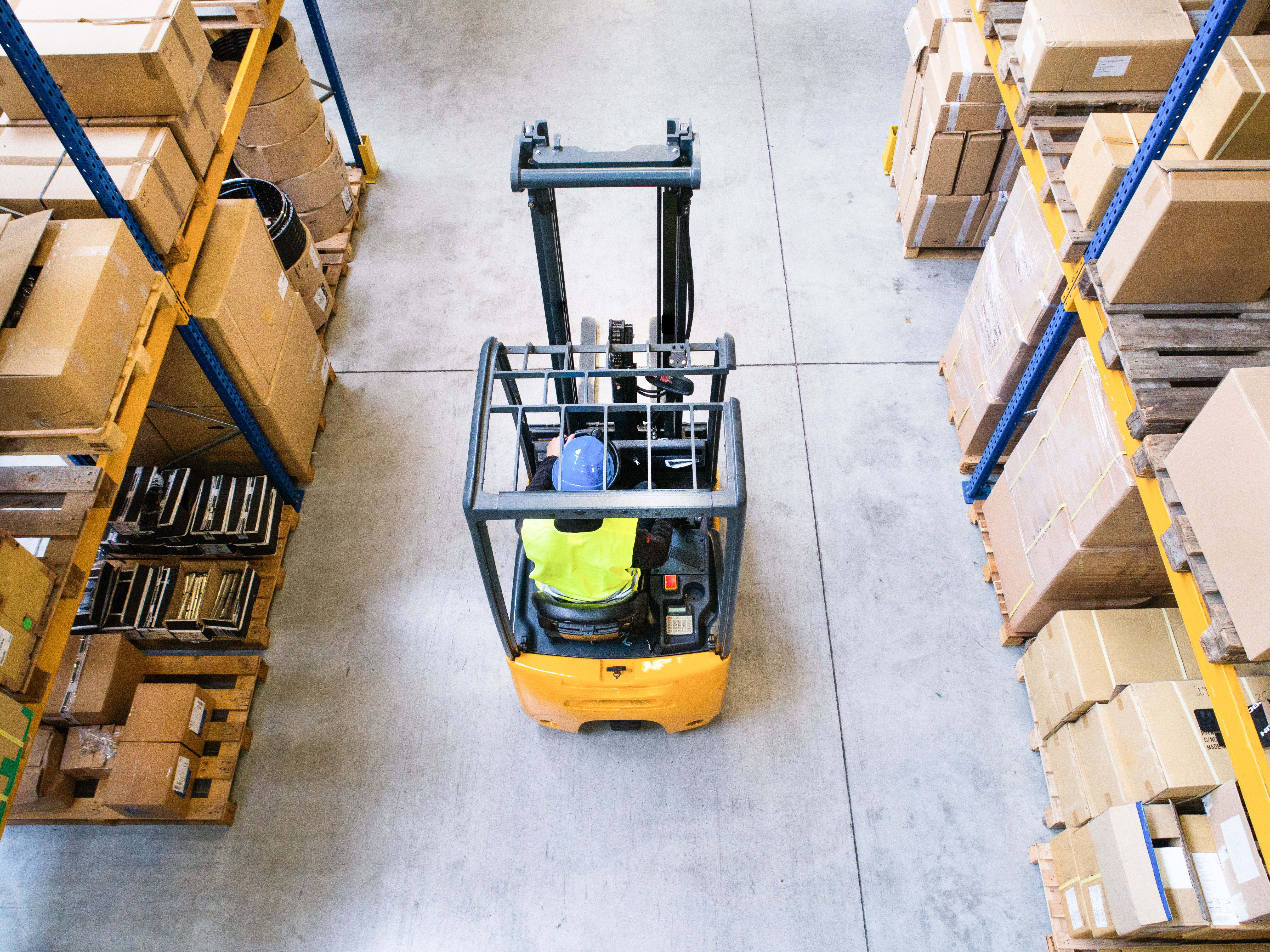 Aerial view of a forklift operating in a large warehouse with concrete floors and shelves stacked with boxes, highlighting grenke's flexible leasing options for diverse forklift fleets and strong UK reseller partnerships.