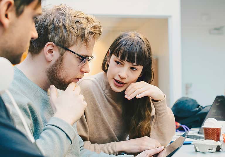Three young professionals in focused discussion using computers, explaining grenke's hire agreement terms, equipment ownership, and hire purchase alternatives