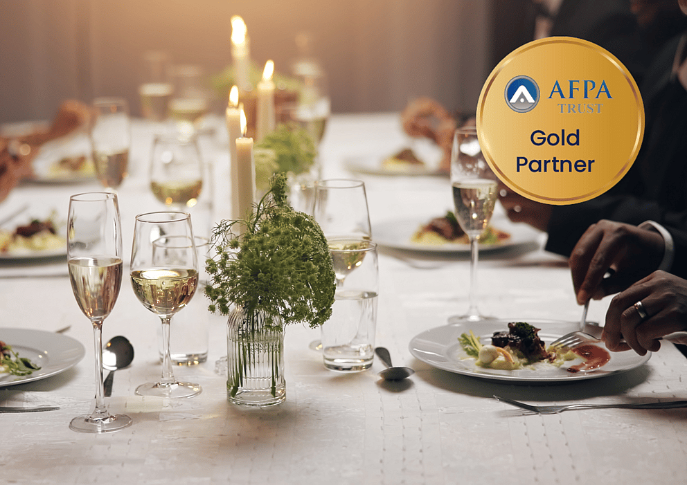 Formal dinner table setting with candles and wine glasses, overlaid with the AFPA Trust Gold Partner emblem.